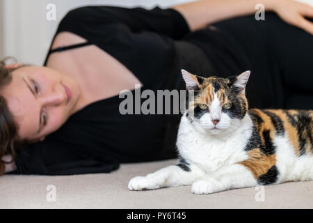 Primo piano di calico Gatto sdraiato sul pavimento moquette insieme con la femmina, donna, proprietario persona accanto, guardando in casa, casa, appartamento camera, amicizia, comp Foto Stock