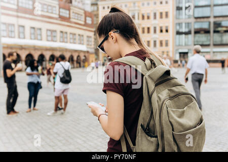 Un turista ragazza con uno zaino o uno studente su una piazza di Lipsia in Germania utilizza un telefono cellulare per visualizzare una mappa o una chiamata o per un'altra. Foto Stock