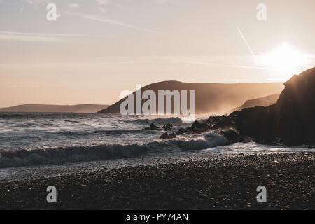 Golden tramonto sulla spiaggia rocciosa vicino Tenby,Pembrokeshire,Galles del Sud, Regno Unito.gli spruzzi delle onde e la brezza della sera,scogliere e la nebbia in background.paesaggio UK. Foto Stock