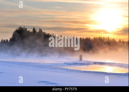 Foschia sopra il fiume di congelamento in un freddo inverno. Vista al tramonto. Foto Stock