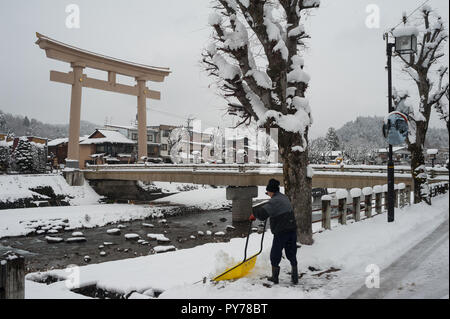 28.12.2017, Takayama, Gifu, Giappone, Asia - un uomo pale neve su una strada accanto alla Miyamae Bashi Bridge con il grande Torii gate ad un lato. Foto Stock