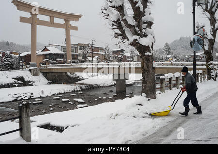 28.12.2017, Takayama, Gifu, Giappone, Asia - un uomo pale neve su una strada accanto alla Miyamae Bashi Bridge con il grande Torii gate ad un lato. Foto Stock