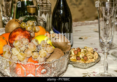 Tabella di festa con frutti in un vaso di cristallo con bottiglie di vino e brandy,dadi,l'uvetta e arachidi Foto Stock