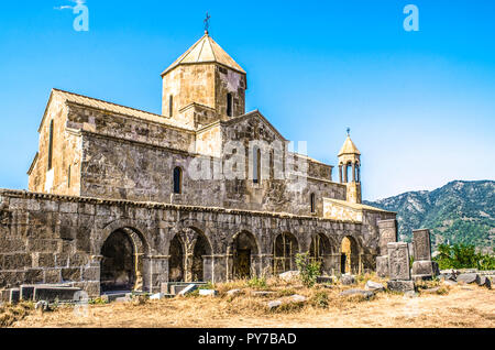 Monastero Odzun sul lato sud con vista della galleria arcuata con la torre campanaria e croci in pietra sullo sfondo di montagne boscose Foto Stock