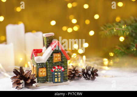 Decorazione del nuovo anno la tabella nella forma di una casa di argilla, candele bianche con ghirlande di spumante su un sfondo dorato. Foto Stock