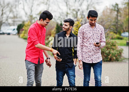 Tre ragazzi indiani gli studenti amici camminando sulla strada e guardando il telefono cellulare. Foto Stock