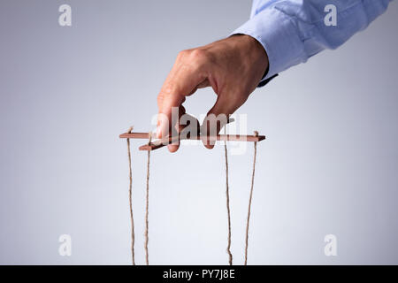 Close-up di mano di una persona la manipolazione di Marionette con stringa su sfondo grigio Foto Stock
