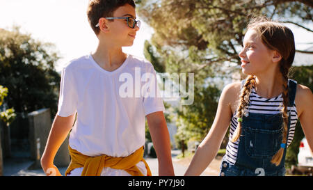 Amore per i bambini a camminare su una strada tenendo le mani guardando ogni altro. Sorridente ragazzo e ragazza camminare sulla strada insieme . Foto Stock