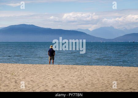 Un uomo in pensione a guardare una bellissima vista sul mare e le montagne. Foto Stock
