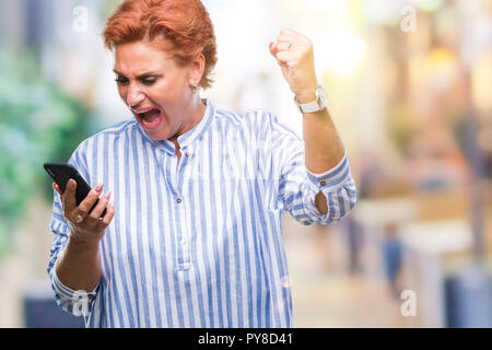 Accattivante senior redhead caucasica donna texting utilizza lo smartphone su sfondo isolato infastiditi e frustrato grida con rabbia, crazy e urlare Foto Stock