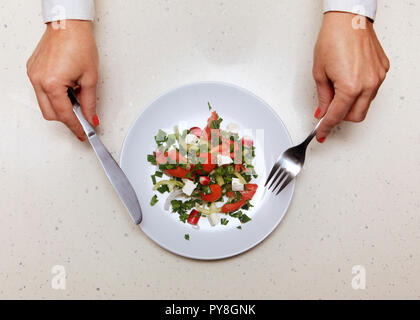 Insalata in piastra bianca, mani del visitatore che trattiene il coltello e forchetta Foto Stock