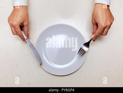 Vuoto piastra bianca, mani del visitatore che trattiene il coltello e forchetta Foto Stock