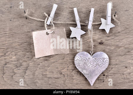 Segno della carta per il messaggio e decorazione di Natale appeso a una stringa su sfondo di legno con cuore metallico Foto Stock