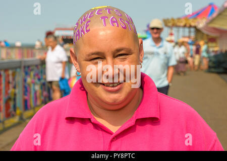 Bald donna con la scrittura sul suo capo cercando di raccogliere fondi per beneficenza a Herne Bay pier, Kent, Inghilterra, Regno Unito. Foto Stock