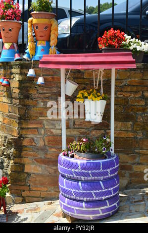 Il pittoresco pentole decorate come due giovani Asturians accanto a un pozzo di acqua anche decorate con pneumatici viola a Taramundi, Asturias, Spagna. Arte e Storia Foto Stock