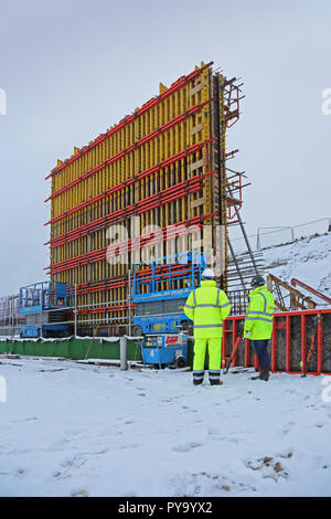 Due lavoratori edili visualizzare un grande edificio sito in Scozia con il lavoro interrotto dalla forte nevicata Foto Stock