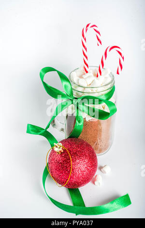 Idea creativa per il regalo di Natale, ingredienti per cioccolata calda (cacao e marshmallow) a mason vasetto in vetro, con verde nastro festoso e albero di natale ba Foto Stock