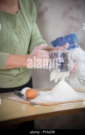 Una vecchia signora rendendo poco torte. Setacciare la farina Foto Stock