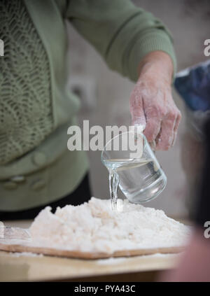 Una vecchia signora rendendo poco torte. Produrre un impasto con versando l'acqua Foto Stock