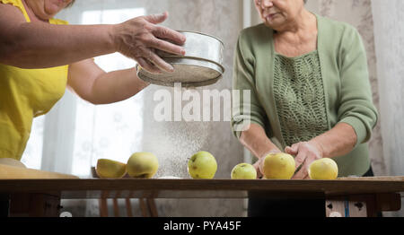 Due donna anziana che rendono Apple poco torte. Setacciare la farina close up Foto Stock