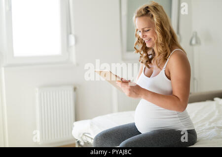 Felice donna incinta utilizzando tablet in camera da letto Foto Stock