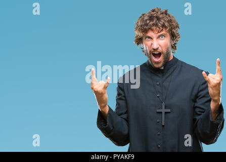 Bello ispanica sacerdote cattolico man over isolato che urlava con crazy espressione facendo il simbolo di roccia con le mani. Stella della musica. Conce pesanti Foto Stock