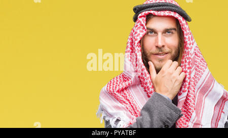 Giovane bello arabian uomo con capelli lunghi che indossa keffiyeh su sfondo isolato guardando fiduciosi alla fotocamera con sorriso con bracci incrociati e h Foto Stock