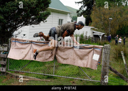 Hunterville, Nuova Zelanda - 27 Ottobre 2018 - un pastore passa al di sopra di una fattoria in anticipo del suo cane in Shemozzle annuale corsa a ostacoli, che vede i canini e pastori tackkle colate di fango, giro in carriole e trasportare i tori di testicoli. Il Shemozzle annuale gara richiama migliaia di persone ogni anno in questa cittadina di meno di 500 persone. Immagine: Giordano Stolley Credito: Giordano Stolley/Alamy Live News Foto Stock