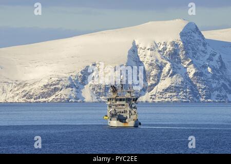 Grigio nave dalla costa norvegese le protezioni nel Mare di Norvegia con le rocce innevate dall'isola Sørøya in background, 9 Marzo 2017 | Utilizzo di tutto il mondo Foto Stock