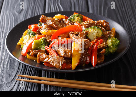 Cibo asiatico: manzo teriyaki con il rosso e il giallo peperoni, broccoli e semi di sesamo close-up su una piastra su una tavola nera orizzontale. Foto Stock