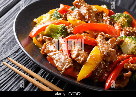 Preparato di fresco piccante asiatici carni bovine teriyaki con il rosso e il giallo peperoni, broccoli e semi di sesamo close-up su una piastra sul tavolo orizzontale. Foto Stock