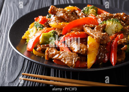 Deliziosi teriyaki asiatici carni bovine con il rosso e il giallo peperoni, broccoli e semi di sesamo close-up su una piastra sul tavolo orizzontale. Foto Stock