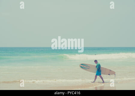 Hikkaduwa Lo Sri Lanka. Marzo 06, 2018. Un surfista passeggiate lungo la spiaggia con una tavola da surf. Foto Stock