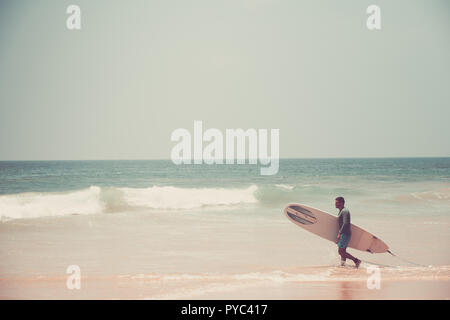 Hikkaduwa Lo Sri Lanka. Marzo 06, 2018. Un surfista passeggiate lungo la spiaggia con una tavola da surf. Foto Stock