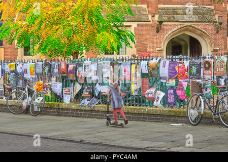 Giovane ragazza cavalca il suo scooter biciclette passato legato alla ringhiera sul marciapiede di St John's Street, al di fuori di St John's College di Cambridge University. Foto Stock