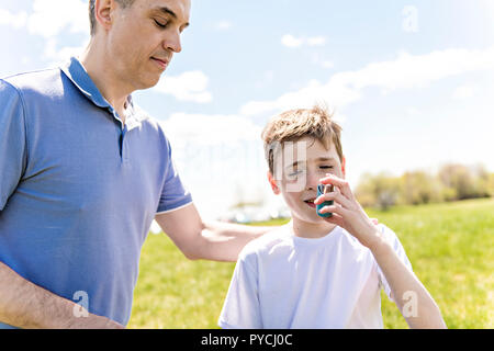 Bambino usando un inalatore per asma al di fuori in un parco con suo padre Foto Stock