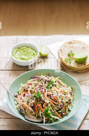 Coleslaw realizzato da verze, carote e varie erbe, servito con tortillas e guacamala su uno sfondo di legno. Messa a fuoco selettiva. Foto Stock