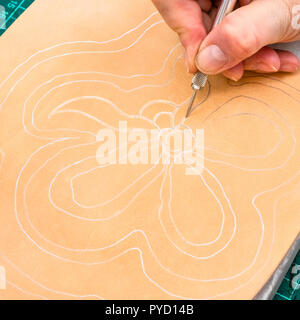 Workshop di rendere incisa la borsa in pelle - artigiano preme il disegno sulla superficie ruvida della pelle conciata al vegetale per il carving da pricker Foto Stock