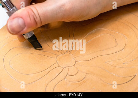 Workshop di rendere incisa la borsa in pelle - artigiano scolpisce motivo floreale sulla superficie ruvida della pelle conciata al vegetale da lama orientabile Foto Stock