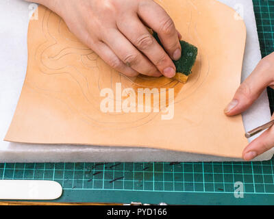 Workshop di rendere incisa la borsa in pelle - artigiano smorza il disegno sulla superficie ruvida della pelle conciata al vegetale prima di timbratura Foto Stock