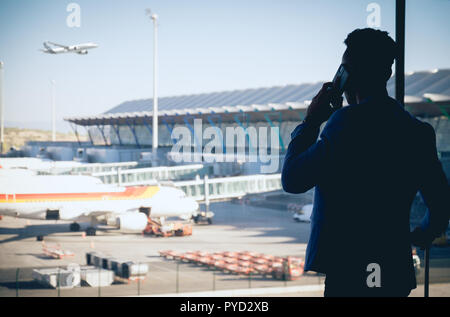 Una giovane e attraente imprenditore è guardando attraverso la finestra nel terminal dell'aeroporto. Un aereo è volare mentre altri sono parcheggiate sulla terra Foto Stock