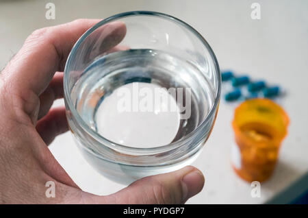 L'uomo tiene con la mano sinistra un bicchiere d'acqua accanto a una pillola bottiglia Foto Stock