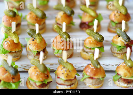 Un delizioso boccone mini hamburger servita su una parte o un ricevimento di matrimonio. Le piastre con fantasia assortiti di finger food snack su un evento parte o la cena. Foto Stock