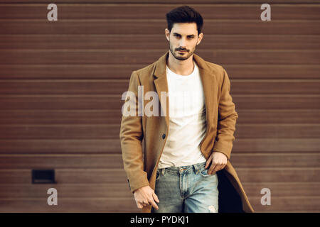 Giovane uomo che indossa abbigliamento invernale in strada. Giovane ragazzo barbuto con moderni acconciatura con rivestimento, jeans blu e bianca t-shirt. Foto Stock