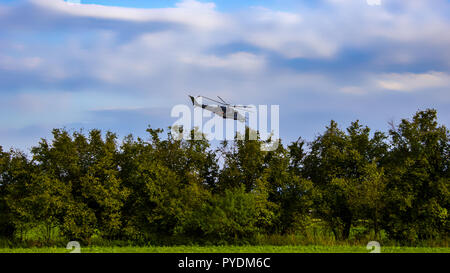 L'elicottero da combattimento sul cielo blu con nuvole bianche. Alberi e la boccola con l'erba. Foto Stock