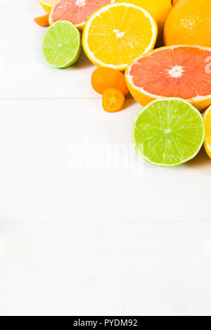 Varie intere e metà agrumi (arancio, limone, calce, pompelmo, kumquat) sul bianco sullo sfondo di legno con spazio di copia Foto Stock
