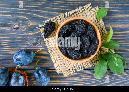 Le prugne secche in un vaso di argilla e prugne fresche, foglie su un tavolo di legno. Prugne fresche per una vita sana. Foto Stock