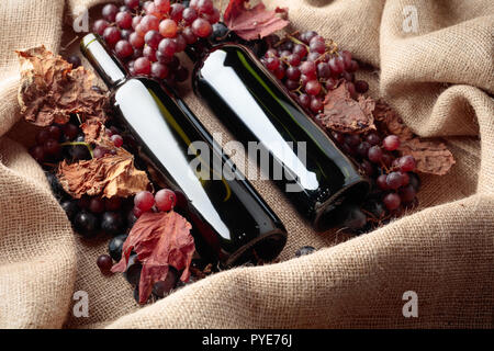 Bottiglie di vino rosso e uve fresche con secchi di foglie di vite su tela. Foto Stock