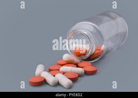 Bianco e arancione pillole sono sparse da una bottiglia di vetro. Foto Stock