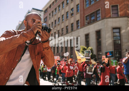 Giovane fotografo prende le immagini degli attivisti holding con segni di slogan. L'uomo prendendo fotografie di un rally su strada della citta'. Foto Stock